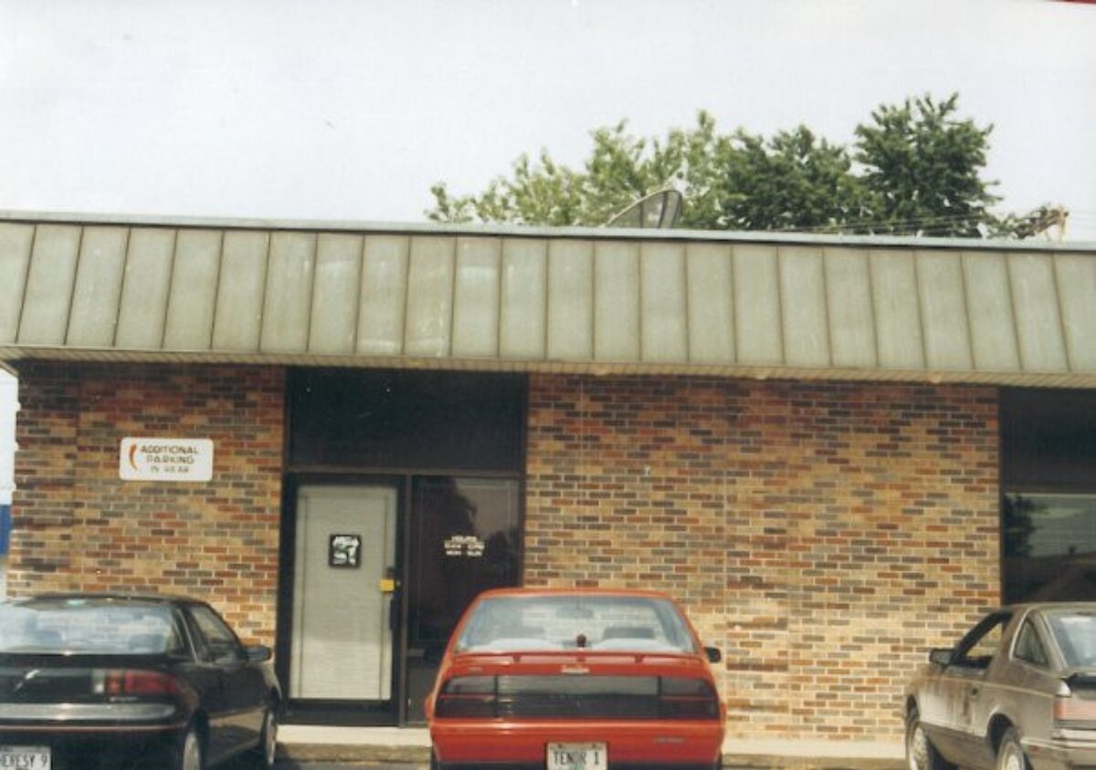 The original Area 51 building in Quincy, Illinois. Single-story brown and tan brick commercial building with a wide overhanging metal cornice roof, glass storefront, and an 'Additional Parking in Rear' sign on the brick.